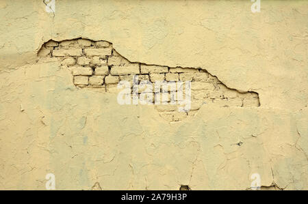 Retro brick wall painted yellow color coated with plaster damaged in centre as conceptual background front view horizontal Stock Photo