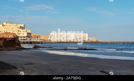 El Medano, Tenerife, Canary Islands, Spain - March 27, 2019: view of the volcanic beach towards the resort hotels, restaurants and terraces Stock Photo