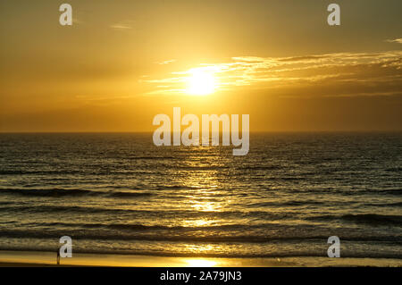 A solitary person watches the sunset from the beach while waves lap gently on the shoreline at Lacanau-Océan, Atlantic coast, France Stock Photo