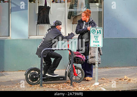 A man on a scooter speaks to an African American woman on a street in downtown Portland, Oregon. Stock Photo