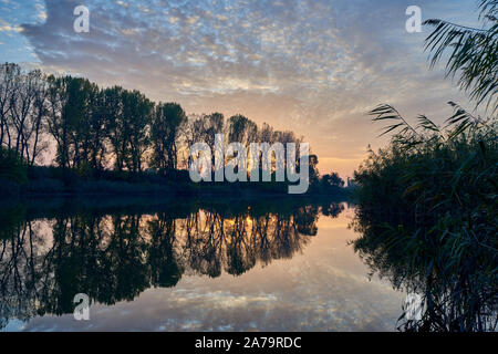 Autumn sunset. Cloudy sky and forest are reflected in the water of the pond. Stock Photo