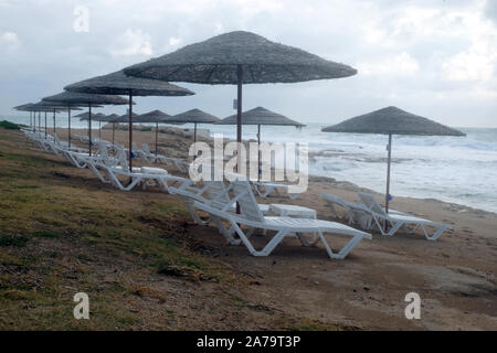 Empty beach on the seaside at the end of resort season with many empty sun loungers and umbrellas in the evening against the backdrop of incoming sea Stock Photo