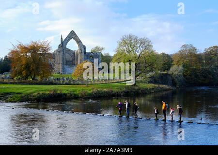 Crossing the stepping stones across the river Wharfe at Bolton abbey ruins in North Yorkshire. UK. Stock Photo