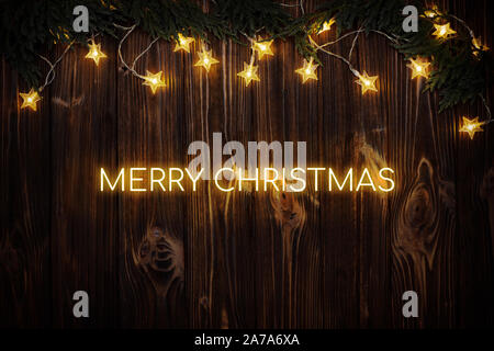 Neon text Merry Christmas on wooden background with fir tree branches and electric garland. Stock Photo
