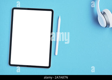 Tablet mockup with white pencil and white wireless headphones on blue background. Top view. Copy space. Stock Photo
