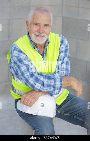 worker in reflective vest and hardhat sitting at construction site Stock Photo
