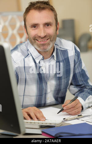 portrait of man at his desk typing and writing Stock Photo
