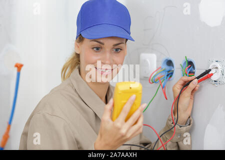 female electrician testing plug socket with multimeter Stock Photo