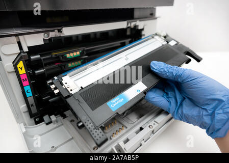 Man replacing toner in laser printer. Hand in gloves holding cyan toner. Stock Photo