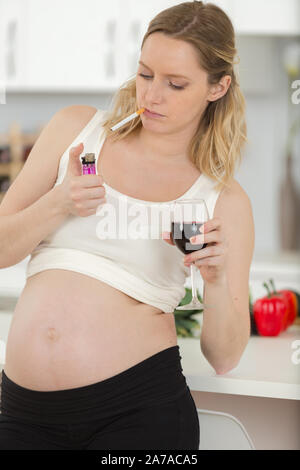 pregnant woman holding glass of wine and lighting cigarette Stock Photo