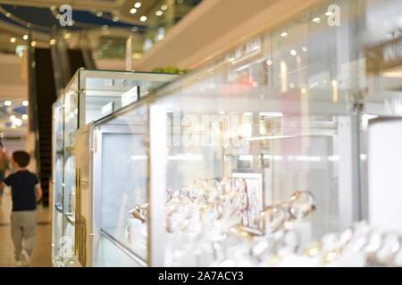 Shop windows on the right, shoppers, escalator in the mall. Stock Photo