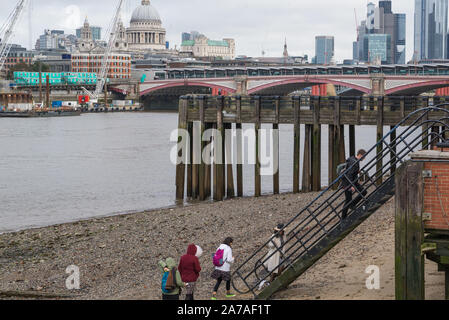 Group of people climbing the stairs from the Thames foreshore at Oxo Tower Wharf, London, England, UK. City of London and St Paul's in background. Stock Photo