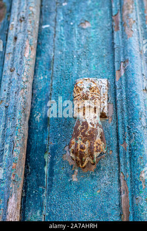 Fragment of an old blue wooden door with shabby paint and a metal rusted hand to knock Stock Photo