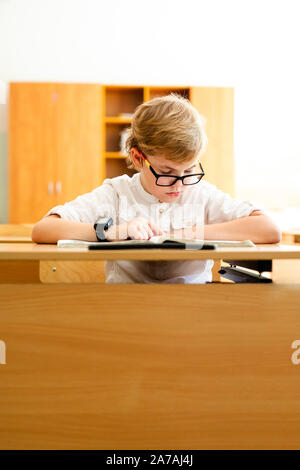 Elementary school student with black glasses writing maths answer on chalkboard. Stock Photo