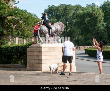 Children having photo taken with mobile phone whilst astride lion statue in Italian Gardens Stanley Park Blackpool Lancashire England UK Stock Photo