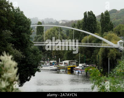 AJAXNETPHOTO. 2019. PORT MARLY, FRANCE. - BRIDGE OVER RIVER SEINE - A NEW PEDESTRIAN AND CYCLIST PASSARELLE BRIDGE CROSSING THE RIVER SEINE AT PORT MARLY TOWERS ABOVE OLD PENICHE HOUSEBOATS MOORED TO THE RIVER BANK. 19TH CENTURY IMPRESSIONIST ARTISTS ALFRED SISLEY, CAMILLE PISSARRO, CLAUDE MONET, AUGUSTE RENOIR, COROT, AS WELL AS FAUVIST EXPRESSIONIST PAINTERS ANDRE DERAIN, MAURICE DE VLAMINCK AND OTHERS MADE STUDIES OF RIVER LIFE NEAR HERE. THE BRIDGE, COMPLETED IN 2016, MEASURES 86M IN LENGTH AND WEIGHS 131 TONNES.PHOTO:JONATHAN EASTLAND/AJAX REF:GX8 192609 554 Stock Photo