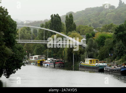 AJAXNETPHOTO. 2019. PORT MARLY, FRANCE. - BRIDGE OVER RIVER SEINE - A NEW PEDESTRIAN AND CYCLIST PASSARELLE BRIDGE CROSSING THE RIVER SEINE AT PORT MARLY TOWERS ABOVE OLD PENICHE HOUSEBOATS MOORED TO THE RIVER BANK. 19TH CENTURY IMPRESSIONIST ARTISTS ALFRED SISLEY, CAMILLE PISSARRO, CLAUDE MONET, AUGUSTE RENOIR, COROT, AS WELL AS FAUVIST EXPRESSIONIST PAINTERS ANDRE DERAIN, MAURICE DE VLAMINCK AND OTHERS MADE STUDIES OF RIVER LIFE NEAR HERE. THE BRIDGE, COMPLETED IN 2016, MEASURES 86M IN LENGTH AND WEIGHS 131 TONNES.PHOTO:JONATHAN EASTLAND/AJAX REF:GX8 192609 560 Stock Photo