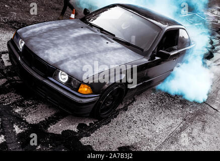 Sport modern Car racing car drifting with smoke drift burnout, big colourful green blue clouds with wheels and burning tires . Extreme street stunts. Stock Photo