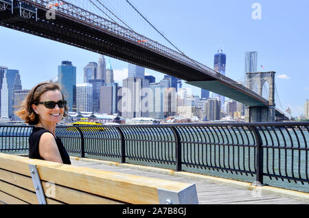 Woman on bench under Brooklyn Bridge, Brooklyn, DUMBO, Empire-Fulton Ferry State Park, East River, Manhattan, New York Stock Photo