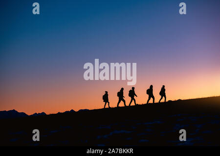 Silhouettes of group of hikers going uphill at sunset mountain Stock Photo
