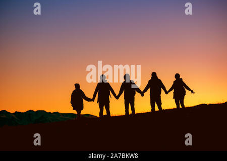 Silhouettes of group of friends are standing together at sunset time against mountains