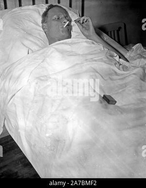 Man in hospital bed smoking a cigarette ca. 1936 Stock Photo