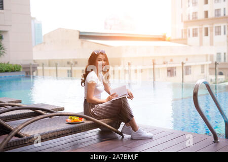 woman reading and relaxing near luxury swimming pool Stock Photo