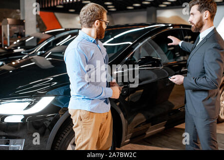 Sales consultant helping the client to choose electric car in the showroom. Concept of selling eco-friendly and modern cars Stock Photo