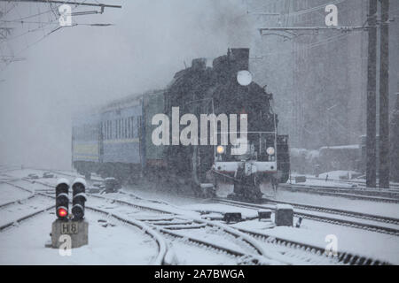 New Year snow railway during a blizzard. Locomotive (puffer) on blurred snowy background is arriving at the station. Winter holiday, railway travel Stock Photo