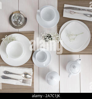 Top view of Table settings in white color, ceramic cups, different plate and silver cutlery with line napkin, teapot,sugar bowl and butter dish on woo Stock Photo