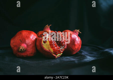 several ripe whole pomegranates and one broken on a dark background Stock Photo
