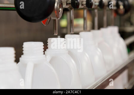 white plastic gallons or bottles on the production line of the conveyor at filling machine in the factory. selective focus. industrial and technology Stock Photo