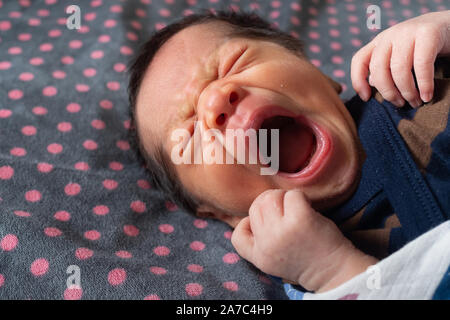 asian newborn baby boy with skin peeling still sleepy and yawning after wake up in the bedroom in the morning with warm sunlight in the summertime. fa Stock Photo