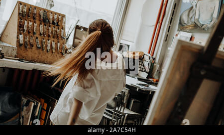 Beautiful female painter wearing white shirt dancing while painting in art workshop. Selective focus. Vintage style photo Stock Photo