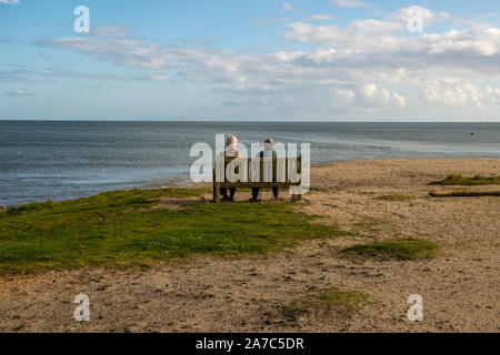 Old couple sitting on a beach bench overlooking the sea Stock Photo