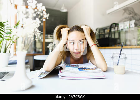 Tired female student sitting at cafe and reading notes. Stock Photo