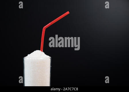 A glass full of white sugar with straw against black background. Concept of unhealthy eating and diabetis Stock Photo