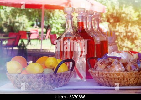 Traditional homemade infused vodka in vintage bottles with fruit and snacks in outdoor cafe. Alcohol drink with red pepper. Summer background and sunl Stock Photo