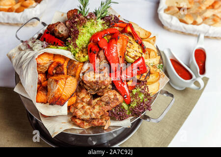 Mixed grill meat, fried vegetables and grilled salmon fish fillets decoration in warm dish. Assorted delicious grilled kebab served with herbs on platter. Restaurant menu plate Stock Photo