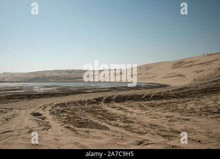 Tourists walk the edge of a dune at the Sealine beach south of Doha in Qatar. Stock Photo