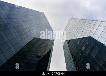 Two skyscrapers made from glass from below with grey cloudy sky Stock Photo