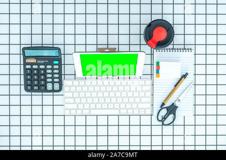 Office and school stationery supplies, reusable cup, keyboard and mobile tablet with green screen on checked background. Business Objects Technology c Stock Photo