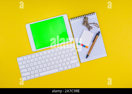 Office School stationery supplies, and mobile tablet with green screen on yellow background. Business Objects Technology, flat lay concept. Stock Photo
