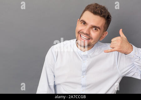 Young man studio standing isolated on grey background showing call gesture looking camera smiling cheerful close-up Stock Photo