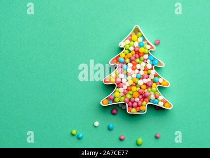 Christmas tree shape made from many colored sweet candies. Creative layout of Christmas tree made of colorful candies over green background. Stock Photo