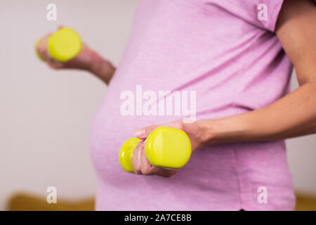 Close Up Of Pregnant Woman Exercising With Weights At Home Stock Photo