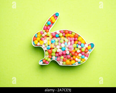 Creative layout of rabbit shape with colorful candies over green background Stock Photo