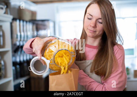 Sales Assistant In Sustainable Plastic Free Grocery Store Weighing Pasta Into Paper Bag Stock Photo