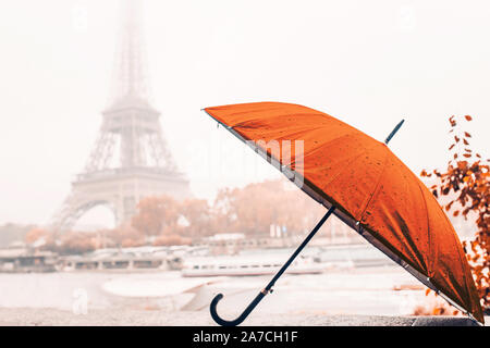 Bright orange umbrella on a rainy autumn foggy day in Paris against the background of the Eiffel tower Stock Photo