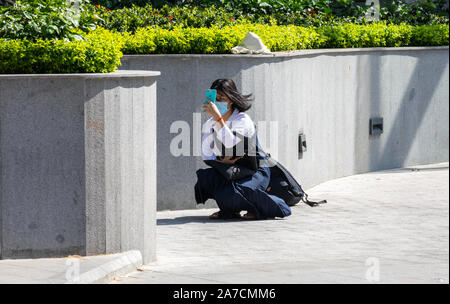 Vietnam, Nha Trang city, March 25, 2019 Vietnamese girl in the mask on the face makes selfie on phone on a Sunny day on the street Stock Photo